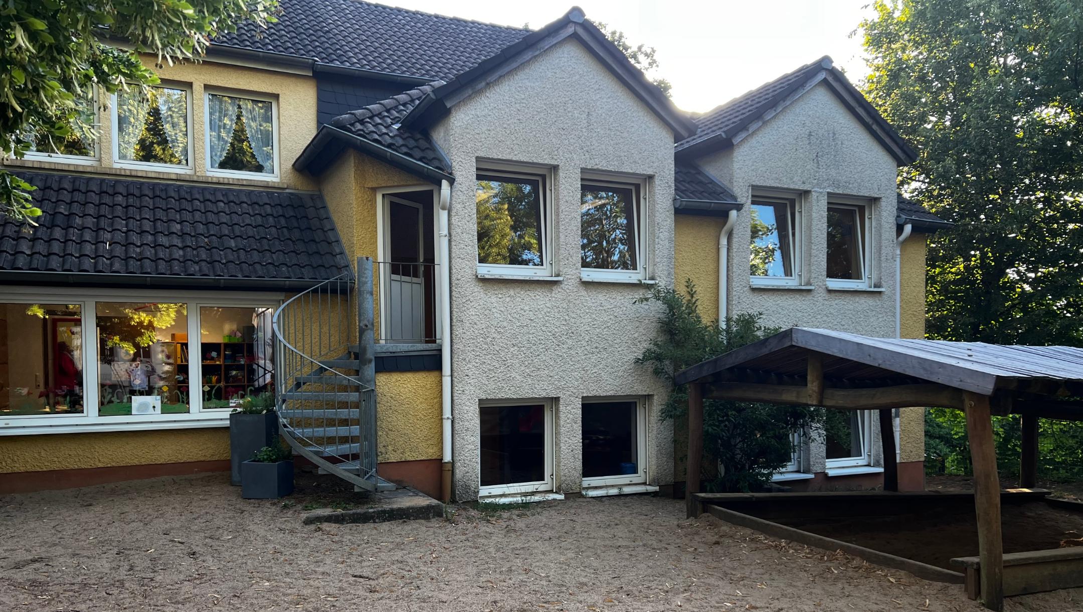 Man sieht das Gebäude mit einer Treppe welche zum Sandkasten führt