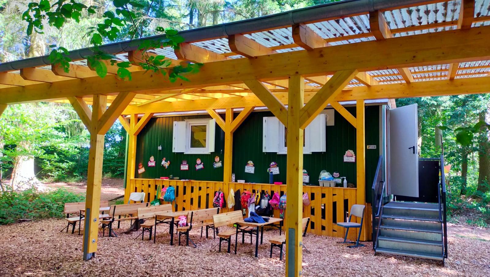 Man sieht einen beschatteten Bereich mit Sitzbänken vor einem Bauwagen