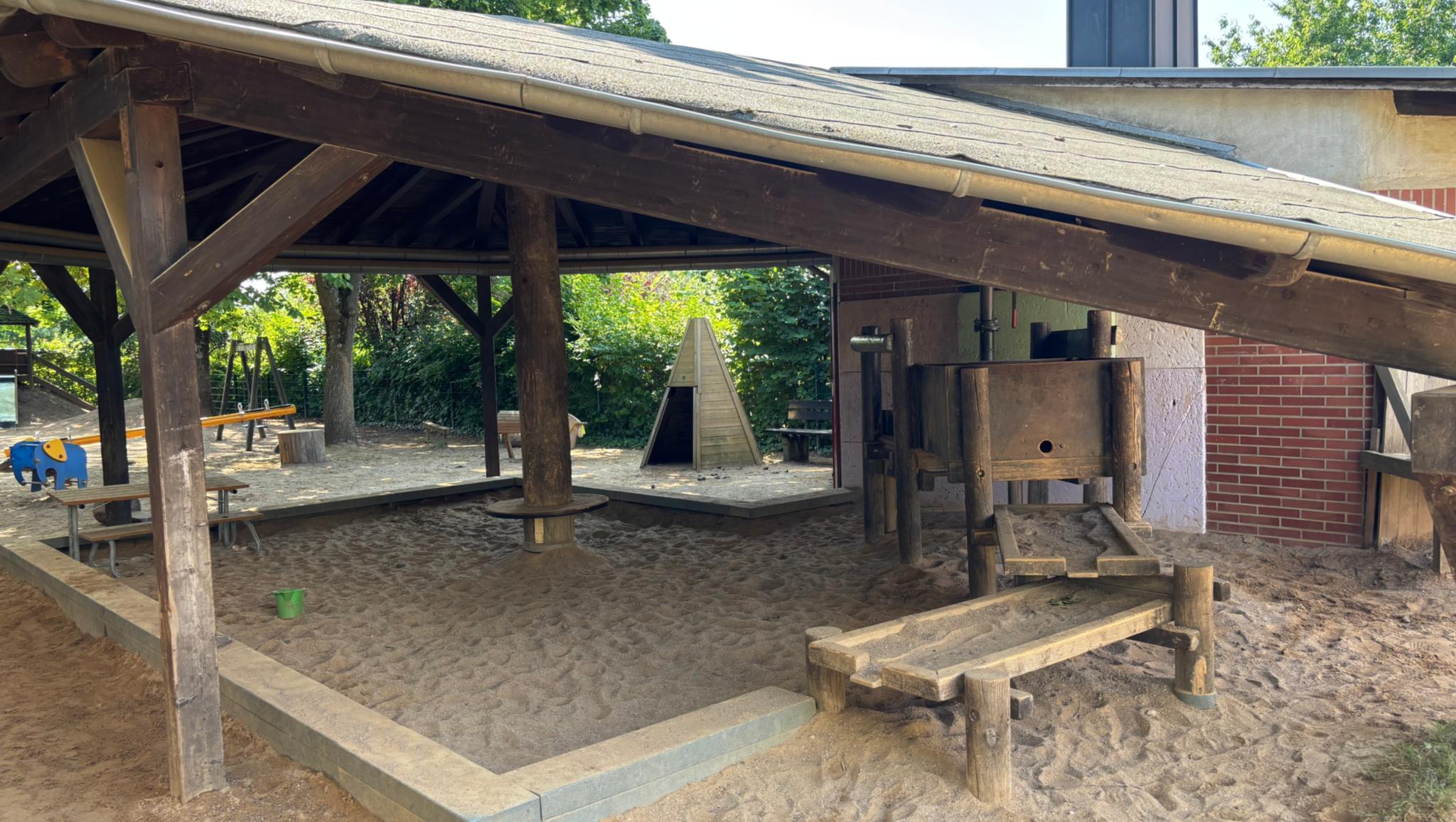 Man sieht den überdachten Sandkasten der KiTa