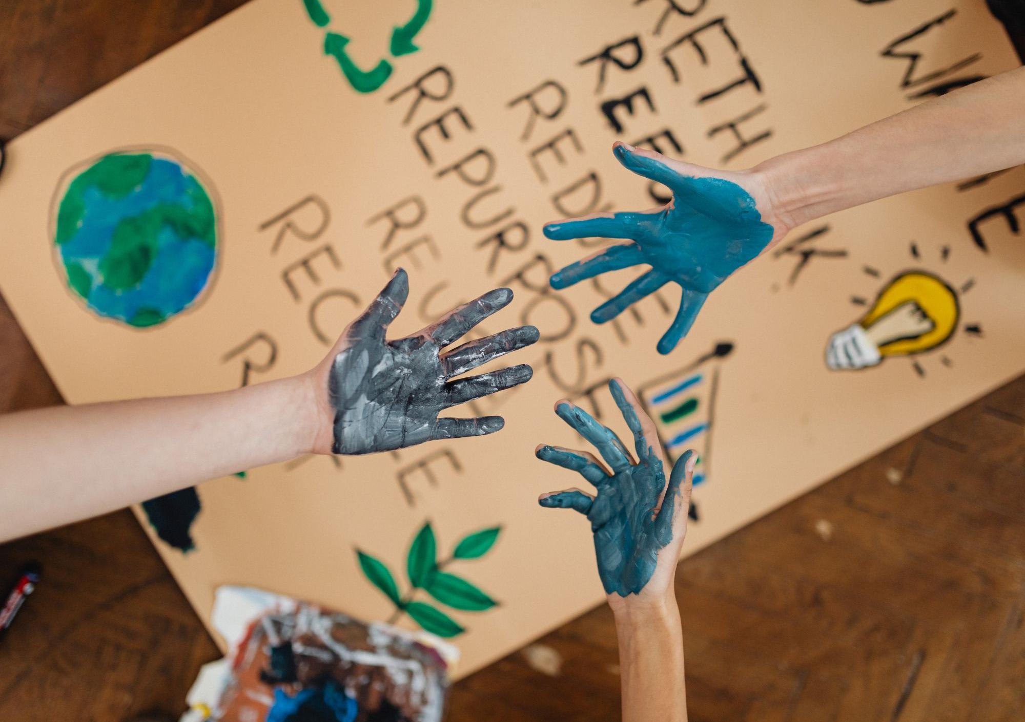 Man sieht mit Farbe bekleckerte Hände und ein BNE Plakat