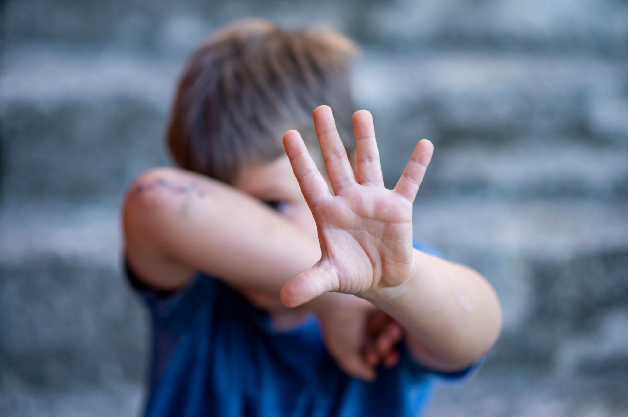 Man sieht ein Kind, welches sich das Gesicht schützt und die Hand ausstreckt, um nein zu sagen